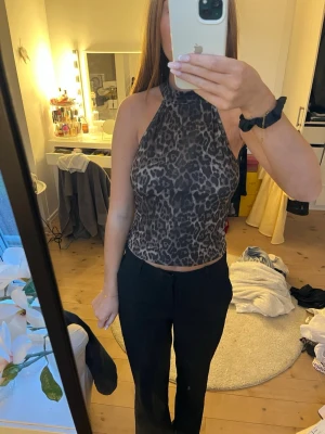 Leopardmönstrad halterneck topp - Säljer en snygg leopardmönstrad halterneck topp i bruna/gråa och svarta toner. Toppen är ärmlös och croppad med hög hals, perfekt för dig som vill sticka ut. Materialet känns mjukt och stretchigt, troligen polyester. Passar till både jeans och kjol.