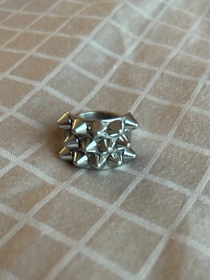 Silvrig Edblad ring - Edbladring i silverfärgad metall. Ringen har en cool design med flera små nitar i tre rader. Perfekt för dig som vill ha en cool och snygg ring att styla till dina outfits. Storlek 17.50