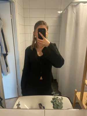 Svart stickad tröja  - Stilren svart tröja  med två knappar framtill och klassisk krage. Kavajen har långa ärmar med knappdetalj vid ärmslut och en rak passform. Perfekt att matcha med svarta byxor för en clean look.