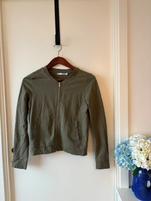 Olivgrön jacka med dragkedja - Snygg och stilren jacka i khakigrön färg med dragkedja framtill. Lättare modell som funkar perfekt som både jacka och tröja - perfekt för lager-på-lager eller som en vardagsfavorit. Har en clean och minimalistisk design med fickor framtill och ribbade detaljer vid ärmslut och nederkant. Enkel att matcha med bade jeans, kostymbyxor eller leggings. Storlek: M Färg: Khaki / olivgrön Skick: Mycket fint skick Sökord: #bomberjacka #grönjacka #khaki #olivgrön #zipup #zipjacka #basic #minimalist #vardag