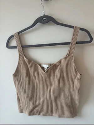 Beige ribbad linnetopp från H&M - Snygg ribbad crop top i beige/nude färg med breda axelband och fin urringning.   perfekt basic-plagg som passar till allt - jeans, kjol eller kostymbyxor.  Stretchigt och bekvämt material som sitter fint på kroppen. Enkel att styla bäde till vardags och fest.  Färg: Beige / nude Modell: Cropped Skick: Mycket fint skick       Sokord: #croptop #beigetop #ribbad #basic #nude #linne #sommartopp #minimalist #vardag #outfit #neutral #capsulewardrobe #basplagg #trend #y2k #streetstyle