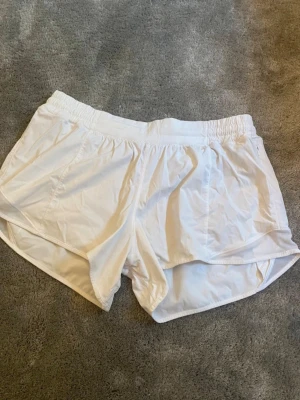Vita träningsshorts från Lululemon - Säljer ett par vita träningsshorts från Lululemon med elastisk midja och innerbyxa. Super snygga tyvärr fel storlek för mig! Inte använda många gånger. 