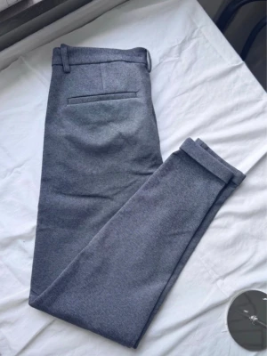 Grå kostymbyxor från Selected Homme - Snygga grå kostymbyxor från Clean Cut Copenhagen med klassisk rak passform. Byxorna har bälteshällor, knapp och dragkedja fram samt två sidofickor och en bakficka. Tillverkade i ett mjukt material som ger en stilren look.