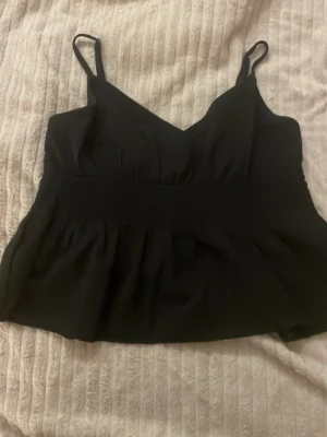 Svart linnetopp - Svart croppad linnetopp med smala axelband och v-ringning. Toppen har en smockad rygg för extra komfort och sitter snyggt på kroppen. Perfekt att styla med jeans eller kjol för en trendig look.är som en M i storlek 
