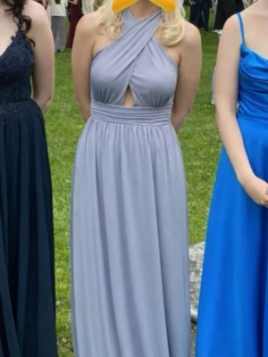 Blå balklänning med omlott - Blå fin långklänning med omlott-detalj upptill och liten cut-out framtill. Klänningen har markerad midja och faller mjukt ner mot golvet. Perfekt för bal. Ärmlös och med halterneck. Endast använd en gång