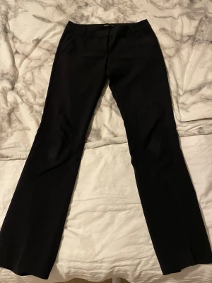 Svarta kostymbyxor från BikBok - Säljer ett par svarta kostymbyxor från BikBok i storlek 34. De är lågmidjade men en knapp har lossnat men det är inget man tänker på och det sitter en i byxorna på lappen som man kan sy ditt 