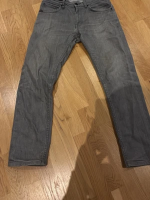 Grå jeans med raka ben - Säljer ett par grå jeans med klassisk femficksdesign och raka ben. Jeansen har knapp- och dragkedjegylf samt dubbla bakfickor. Materialet är denim och färgen är en snygg grå nyans som passar till det mesta.