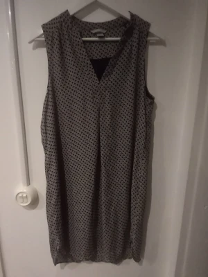 Svartvit mönstrad låg linne H&M - Svartvit ärmlös lång linne från H&M med v-ringning och grafiskt mönster. Lätt och luftig modell som slutar ovanför knäna, perfekt för varmare dagar. Tillverkad i ett mjukt och bekvämt material.