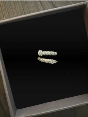 Silverfärgad ring med gnistrande stenar - Unik silverfärgad ring i spiralform med massor av små gnistrande stenar över hela ytan. Ringen har en modern design där ändarna liknar en spik och är täckta av stenar som ger extra bling. Perfekt för dig som vill sticka ut med dina accessoarer.