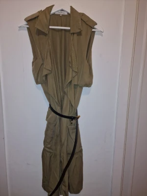 Khaki trenchcoat från Zara - Ärmlös kappa med snygg siluett och draperad front. Perfekt för lager på lager och trendiga outfits. Det svarta skärpet ingår ej.