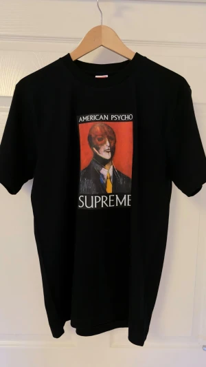 Supreme American Psycho T-shirt svart - Svart Supreme T-shirt med tryck av American Psycho-motiv på bröstet. Klassisk passform med korta ärmar och rund hals. Tillverkad i 100% bomull. Perfekt statement-plagg. Nytt skick