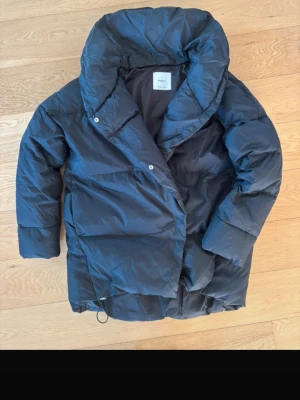 Svart pufferjacka från Mango - Säljer en svart pufferjacka från Mango med hög krage och dragkedja samt tryckknappar framtill. Jackan har en oversized look och justerbar dragsko nedtill. Perfekt för kalla vinterdagar och riktigt snygg till streetwear-stilen.