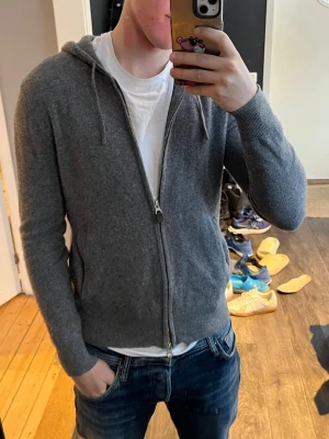 Grå zip hoodie i 100% kashmir - Mysig grå hoodie med dragkedja och huva i 100% Kashmir. Klassisk modell med ribbade muddar vid ärmslut och nederkant samt dragsko i huvan. Perfekt till jeans eller joggers för en chill look. storleken är S men sitter mindre som xs
