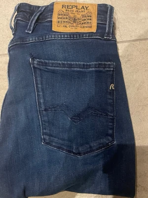 Mörkblå jeans från Replay - Snygga mörkblå jeans från Replay med klassisk femficksmodell och raka ben. Jeansen har en läderpatch med Replay-logga bak i midjan och diskreta slitningar framtill. Tillverkade i mjuk denim som ger en skön passform.  Har en lite defekt vid knät som inte märks till