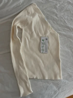 Ribbad offshoulder topp i beige - Trendig ribbad offshoulder topp i beige med lång ärm. Snygg croppad passform och stretchigt material som sitter skönt på kroppen. Perfekt för dig som vill ha en unik och stilren look.