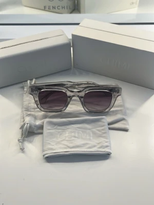 Solglasögon från Chimi - Säljer ett par stilrena solglasögon från Chimi med transparent, fyrkantig båge och mörktonade glas. Kommer med originalfodral och tygpåse. Perfekta för dig som vill ha en modern och clean look.