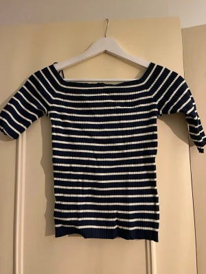 Randig ribbad topp från Zara - Säljer en marinblå och vit randig topp från Zara. Toppen är ribbad, har en lite halft offshoulder urringning och trekvartsärm. Perfekt för dig som gillar en stilren och trendig look. Materialet är stretchigt och bekvämt. Tröjan är endast testad o säljer då de inte kommer till användning. Mindre i storleken oxå, står L men skulle säga att den sitter som en M. Pris kan diskuteras