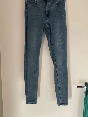 Blå slim fit jeans med hög midja M  - Snygga blå slim fit jeans med hög midja och klassisk femficksdesign. Jeansen har smal passform hela vägen ner och är tillverkade i ett mjukt denimtyg med lite stretch för extra komfort. Perfekta till en avslappnad look.
