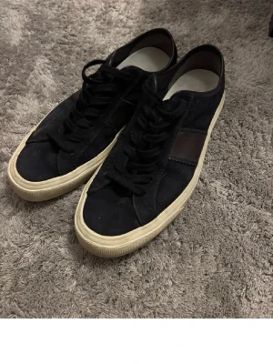 Tom Ford marinblå mocka sneakers  - Snygga marinblå Tom Ford sneakers i mocka med vit gummisula och svart läderdetalj på sidan. Klassisk låg modell med marinblå skosnören och diskret design som passar till det mesta. Perfekta för dig som gillar stilrena och tidlösa skor.