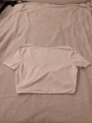 Vit topp - Säljer en vit croppad topp med omlottdetalj baktill. Toppen har korta ärmar och en djup v-ringning. Perfekt för dig som gillar en enkel men trendig stil.