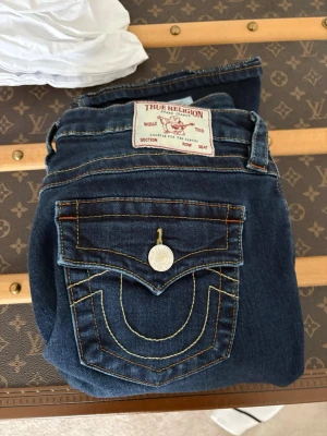 Mörkblå True Religion jeans bootcut - Säljer ett par mörkblåa true religion jeans, midjan är i storlek 29 men är lite små i storlek skulle jag säga, jag sydde upp jeansen så dom passar mig som är 165cm lång. Använd 1-2 gånger och köptes på Nk för ca 1200kr