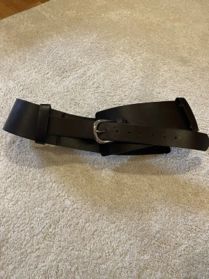 Brett mörkbrunt skärp  - Snyggt och brett mörkbrunt skärp  med silverfärgat spänne. Perfekt för att ge extra edge till din outfit. Stilren design utan mönster och passar till många olika looks.