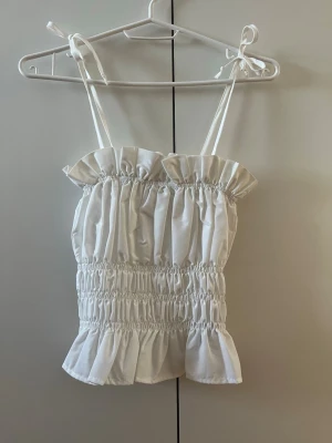 Vit volangtopp med knytband - Topp från Gina Tricot i storlek 32, men passar mer 34-36. Knytningen på axlarna går att justera. 