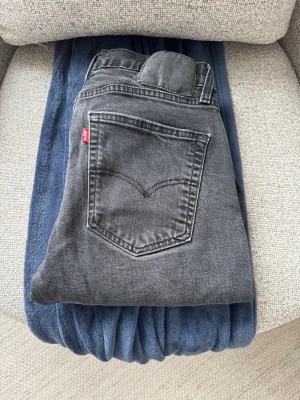 Svarta Levi's jeans med rak passform - Säljer ett par svarta Levi's jeans med klassisk rak passform och femficksmodell. Jeansen har en diskret tvättad look och den ikoniska röda Levi's-lappen på bakfickan. Perfekta för dig som gillar en tidlös och avslappnad stil.