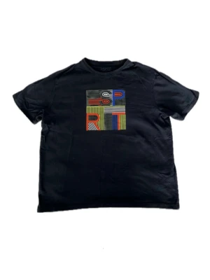 Svart t-shirt från Esprit med tryck - Svart t-shirt från Esprit med färgglatt grafiskt tryck på bröstet där det står 'ESPRIT' i olika färger och ränder. Klassisk rund hals och korta ärmar. Storlek L/164/14 år men passar som en S vuxenstorlek.