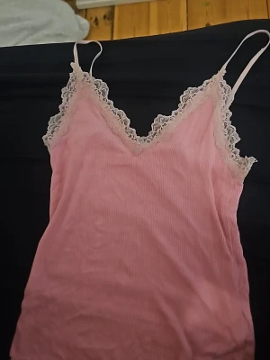 Rosa linnetopp med spetsdetaljer - Söt rosa linnetopp med tunna axelband och v-ringning. Toppen har fina spetsdetaljer längs urringningen och ärmlösa kanter. Perfekt för en trendig och feminin look. Pris kan diskuteras.