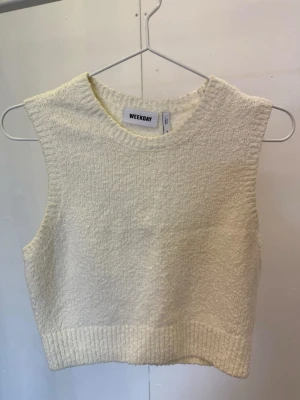 Crèmevit ärmlös topp från Weekday - Säljer en stilren vit ärmlös topp från Weekday. Toppen har en croppad passform och är gjord i ett mjukt, stickat material med struktur. Perfekt att matcha med höga jeans eller kjol för en trendig look.