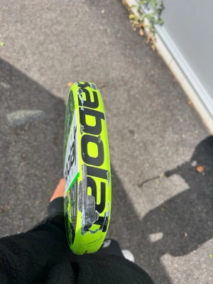 Gul Babolat Counter padelracket - Säljer ett Babolat Counter padelracket i neon-gult med svarta detaljer. Racketen har en rund form och är tillverkad i kompositmaterial. Perfekt för dig som vill ha kontroll och kraft i spelet. Snygg design och tydlig logga på sidan.