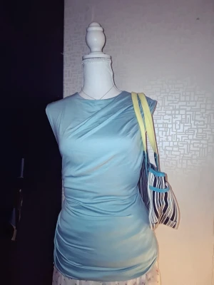 Turkos topp  - Trendig ljusblå topp i satinliknande material med oneshoulder-design. Toppen har en tight passform och kan bäras både som vanlig topp eller offshoulder. Perfekt för dig som vill ha en stilren och modern look. Large men passar mer som en Medium