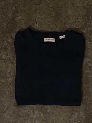 Mörkblå tröja från Jack & Jones - En stilren mörkblå tröja från Jack & Jones med rund halsringning och långa ärmar. Perfekt basplagg i garderoben, enkel att matcha och passar till många olika looks. Tillverkad i mjukt material för skön känsla.