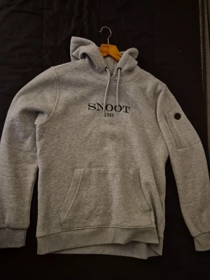 Snoot hoodie - Snygg grå hoodie från Snoot m med svart logga på bröstet och en liten broderad fågel på huvan. Tillverkad i mjukt sweatshirtmaterial, lite schysstare!