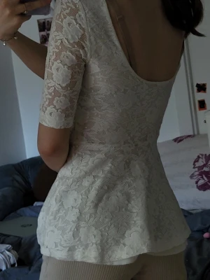 Vit spetsblus med halvlånga ärmar - Säljer en söt vit blus i spets med blommigt mönster och halvlånga ärmar. Blusen har en djup rygg och sitter figurnära upptill med en lätt utsvängd nederdel. Perfekt för dig som gillar romantisk och feminin stil.