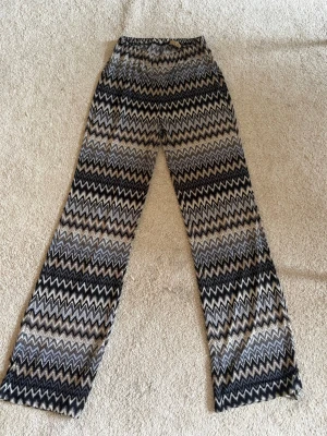Mönstrade vida leggings i zigzag - Säljer ett par snygga leggings med vida ben och zigzag-mönster i svart, grått och beige. De har resår i midjan och är tillverkade i ett mjukt, stretchigt material som sitter skönt. Perfekta för dig som gillar retrovibbar och vill sticka ut lite extra.