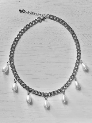 Kedjehalsband med droppformade pärlor - Snyggt halsband med grov silverfärgad kedja och sju droppformade vita pärlor som hänger längs kedjan. Halsbandet har justerbar längd med förlängningskedja och karbinlås. Perfekt för att ge din outfit en trendig touch.