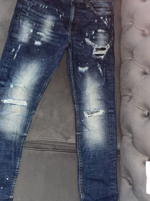 Distressed jeans från Supply & Demand - Säljer ett par blå distressed jeans från Supply & Demand. De har slitningar, hål och blekta detaljer framtill för en riktigt trendig streetlook. Klassisk femficksmodell med dragkedja och knapp. Perfekta för dig som gillar en edgy stil.