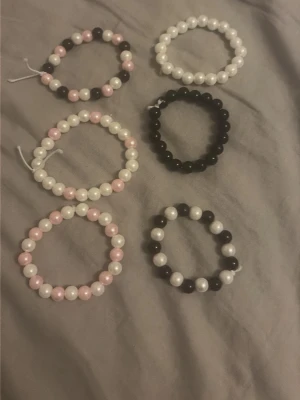 Set med pärlarmband i svart, vitt och rosa - 6 armband Säljer ett set med sex elastiska armband gjorda av pärlor i färgerna svart, vitt och ljusrosa. Armbanden har rund form och varierar i färgkombinationer, vissa är enfärgade och andra mixar färgerna. Perfekta för att addera en söt touch till din stil. Olika storlekar på dem 