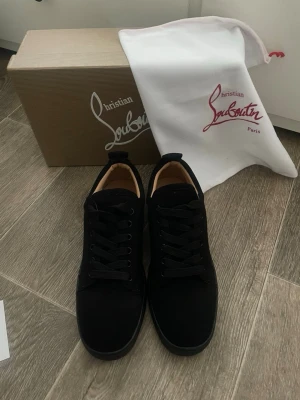 Svarta sneakers från Christian Louboutin - Stilrena svarta sneakers från Christian Louboutin i mocka med klassisk röd sula och svarta skosnören. Låg modell med diskret design och exklusiv känsla. Perfekta för dig som vill ha något lyxigt och tidlöst i garderoben.
