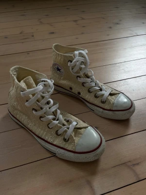 Broderade Converse All Star highs - Unika Converse All Star sneakers i high-top modell med ljusgul/krämvit färg och broderade detaljer. Klassisk vit gummisula med röd rand och vita skosnören. Converse-logga på sidan och snygg retrostil som sticker ut.