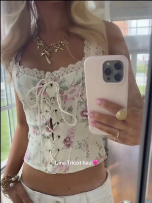 Blommig top - Helt ny oanvänd Supersöt korsettopp med blommigt mönster i ljusa pastellfärger från Gina Tricot. Toppen har snörning framtill, spetsdetaljer längs urringningen och är ärmlös. Perfekt för dig som vill ha en romantisk och trendig look.