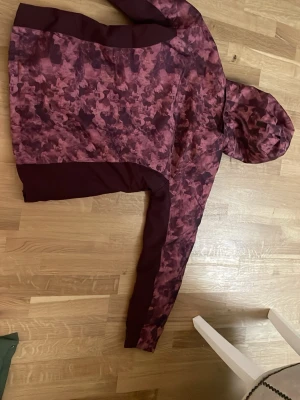 Vinröd camo vindjacka med huva - Snygg vindjacka i vinrött med camomönster och hel dragkedja framtill. Jackan har huva och två sidofickor med dragkedja. Perfekt för blåsiga dagar och har en sportig look. Märke: North Bend.