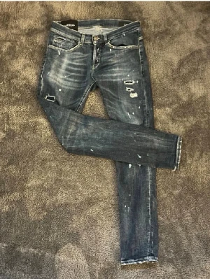Dondup George jeans slim fit - Snygga blå jeans från Dondup, modell George Skinny Fit. De har slitna detaljer, blekta partier och coola små revor för en edgy look. Klassisk femficksdesign, smal passform och tillverkade i stretchig denim för extra komfort. Köptes på Nääs fabriker för runt 4000. Använd fåtal gånger, nyskick. De här byxorna är otroligt limiterade. Skriv vid intresse👍