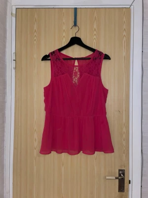 Rosa ärmlös blus med spetsdetaljer - en söt rosa blus med spetsdetaljer upptill och v-ringning. Blusen är ärmlös och har en lätt volang nedtill samt transparent tyg över axlar och rygg. Perfekt för dig som gillar feminina och luftiga toppar.