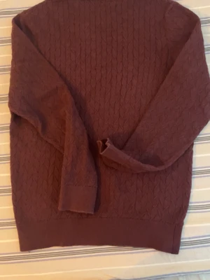 Vinröd stickad tröja från Dressmann - Säljer en vinröd stickad tröja från Dressmann med snyggt strukturmönster. Tröjan har rund halsringning, långa ärmar och ribbade muddar vid ärmslut och nederkant. Perfekt för dig som gillar stilrena och bekväma plagg.