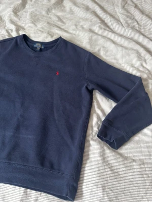 Polo Ralph lauren marinblå tröja Xs - Klassisk marinblå sweatshirt från Polo Ralph Lauren med rund halsringning och diskret röd logga broderad på bröstet. Tröjan har långa ärmar och är tillverkad i mjukt bomullsmaterial. Perfekt för en avslappnad och stilren look.