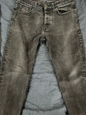 Svarta slim fit jeans från Diesel - Säljer ett par svarta slim fit jeans från Diesel med slitna detaljer och klassisk femficksmodell. Jeansen har en diskret logga på myntfickan och bakfickan. Materialet är stretchigt denim som ger en bekväm passform.