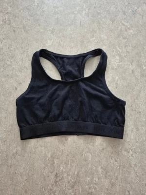 Sport-behå - En enkel svart sport-bh med brottarrygg och bred resår under bysten. Tillverkad i mjukt och stretchigt material som ger bra stöd vid träning. Inga vadderingar eller byglar, perfekt för dig som vill ha en bekväm och stilren look.